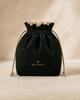 A dark forest green corduroy drawstring pouch with a beige ruffled trim and beige drawstrings, featuring the brand name 'MILOUA' embroidered in gold on the front, set against a warm beige textured background.